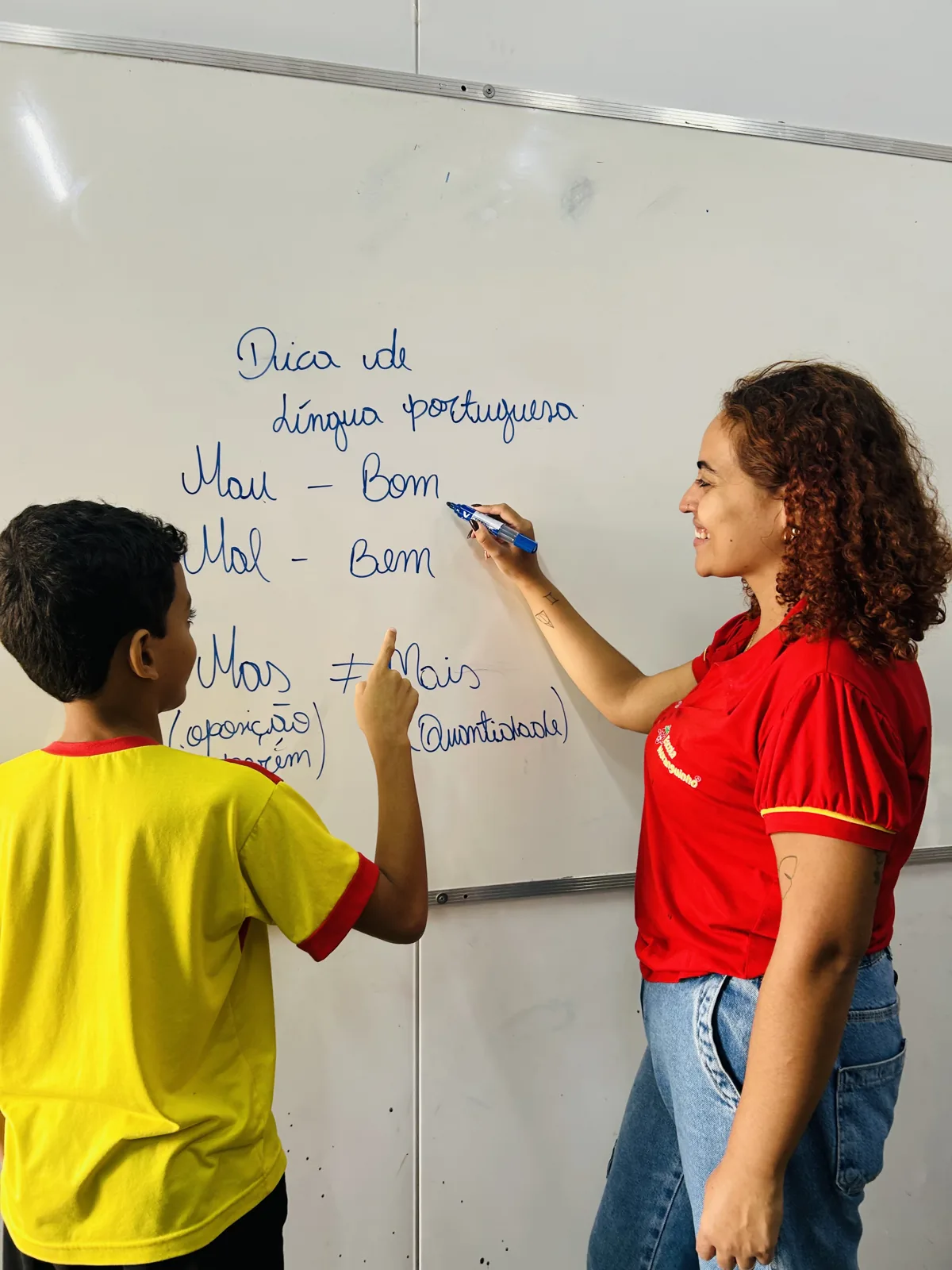 Professora acompanha aluno em atividade de escrita no quadro